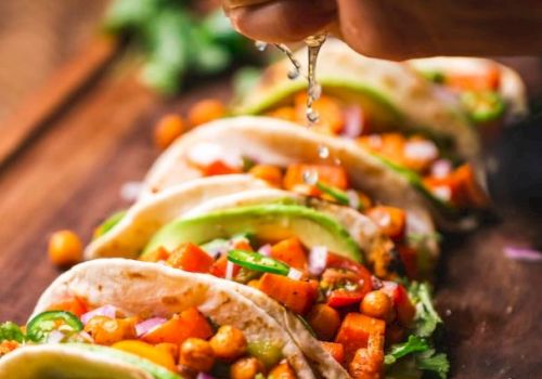 Tacos garnished with vegetables and chickpeas, topped with lime juice being squeezed over them on a wooden board.