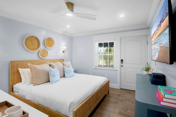A cozy bedroom with a bed, decorative baskets on the wall, TV, books, and a window letting in natural light, creating a serene ambiance.