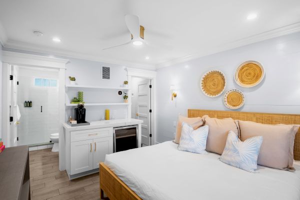 A bright bedroom with a bed, decorative wall baskets, a kitchenette, and an open bathroom door in a modern design setting.
