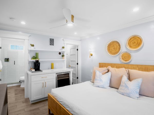 A bright bedroom with a bed, decorative wall baskets, a kitchenette, and an open bathroom door in a modern design setting.