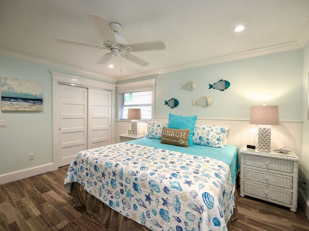 A beach-themed bedroom with fish decor, a cushy bed, and stylish lamps, evoking a coastal vibe in soft blue and white tones.