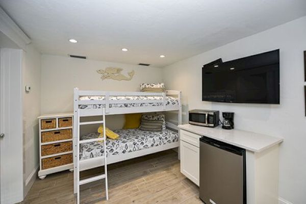 The image shows a room with a bunk bed, storage unit, TV, microwave, coffee maker, mini fridge, and a counter.