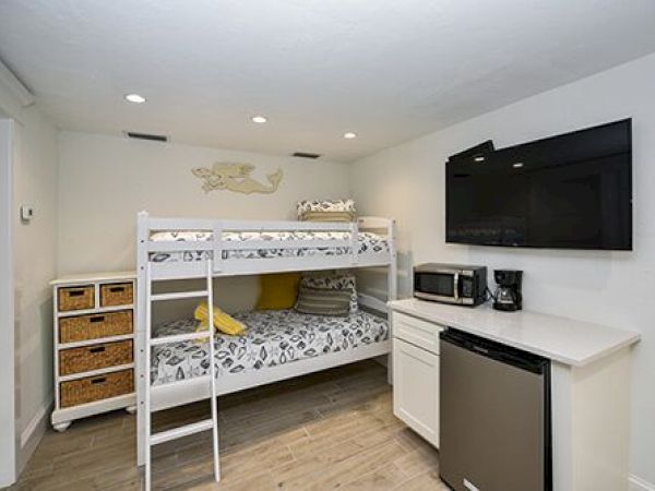 The image shows a room with a bunk bed, storage unit, TV, microwave, coffee maker, mini fridge, and a counter.