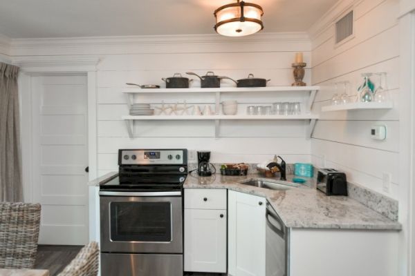 A cozy kitchen with white cabinets, open shelves, a stainless-steel stove, coffee maker, toaster, dishes, and cookware on display.