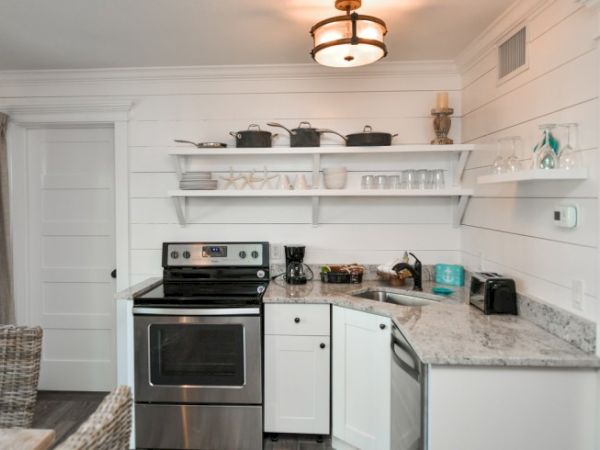 A cozy kitchen with white cabinets, open shelves, a stainless-steel stove, coffee maker, toaster, dishes, and cookware on display.