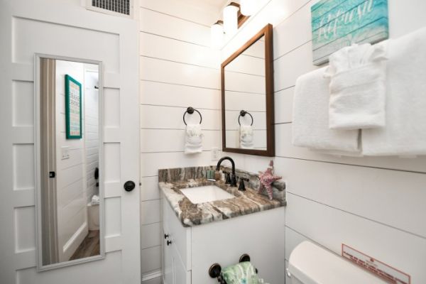 Bathroom with a vanity, mirror, towels, starfish decor, and a door with a full-length mirror. The style is modern and clean.