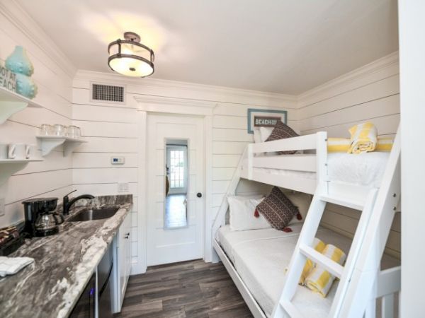A cozy room features white bunk beds, a compact kitchen with a marble counter, and decorative beach-themed accents on the walls.