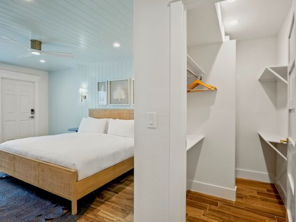 A modern bedroom with a wooden bed, white linens, open closet, wooden floor, and minimal decor is shown.