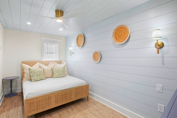 A cozy bedroom with a wicker bed, decorative wall plates, and a ceiling fan. Light blue walls and wooden flooring complete the serene look.