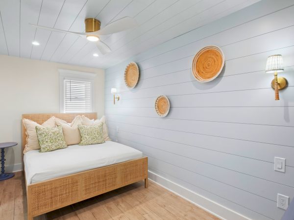 A cozy bedroom with a wicker bed, decorative wall plates, and a ceiling fan. Light blue walls and wooden flooring complete the serene look.