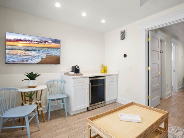 A cozy room features a small dining area, kitchenette, and TV, with soft lighting and wooden floors, creating a welcoming atmosphere.