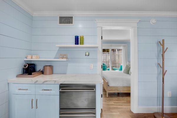 A cozy corner with a countertop, coffee maker, shelves, and entryway to a bedroom, painted in soft pastels.