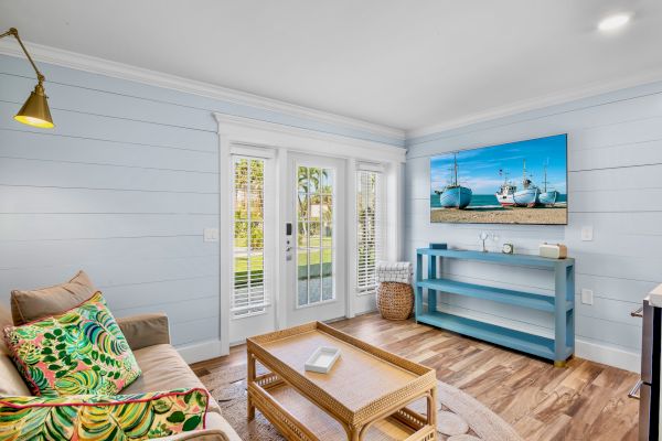 A cozy living room with light blue walls, a sofa with colorful cushions, a wicker coffee table, and a TV displaying boats.