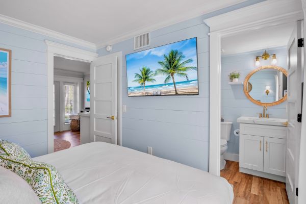 A coastal-themed bedroom with a TV showing a beach scene, a bathroom with a round mirror, and white-and-blue decor ending the sentence.