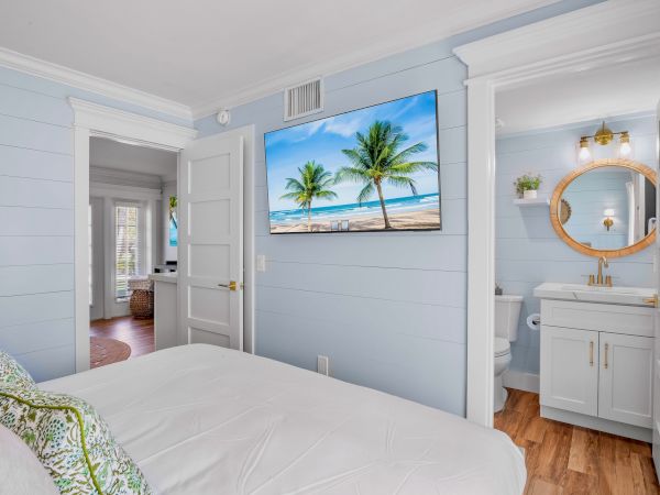 A coastal-themed bedroom with a TV showing a beach scene, a bathroom with a round mirror, and white-and-blue decor ending the sentence.