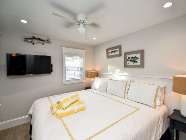 A cozy bedroom with a large bed, wall-mounted TV, ceiling fan, and fish-themed decor, featuring neatly arranged yellow towels on the bed.