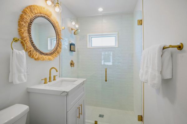 A modern bathroom with gold fixtures, a marbled vanity, and a unique round mirror with straw detailing adorn the wall.