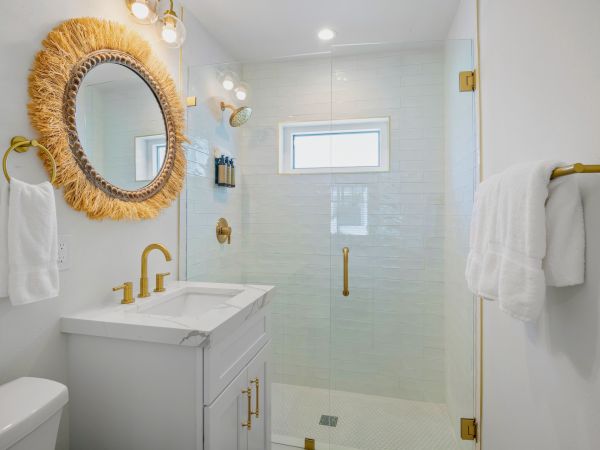 A modern bathroom with gold fixtures, a marbled vanity, and a unique round mirror with straw detailing adorn the wall.