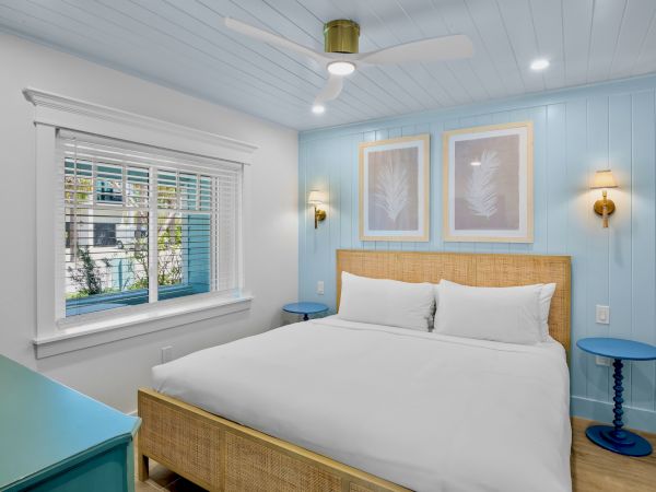 A cozy bedroom with light blue walls, a large bed, simple framed art, two bedside tables, and a ceiling fan above.