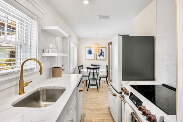 A modern kitchen and dining area with white cabinets, marble countertop, gold faucet, black dining chairs, and framed art.