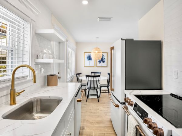 A modern kitchen and dining area with white cabinets, marble countertop, gold faucet, black dining chairs, and framed art.