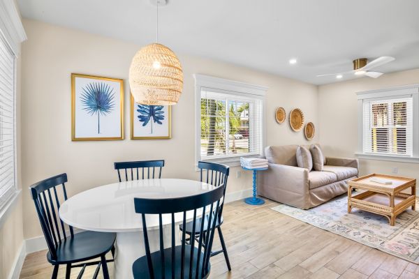 A bright living room with a sofa, wicker coffee table, dining set, and wall decor. Light decor creates an inviting space.