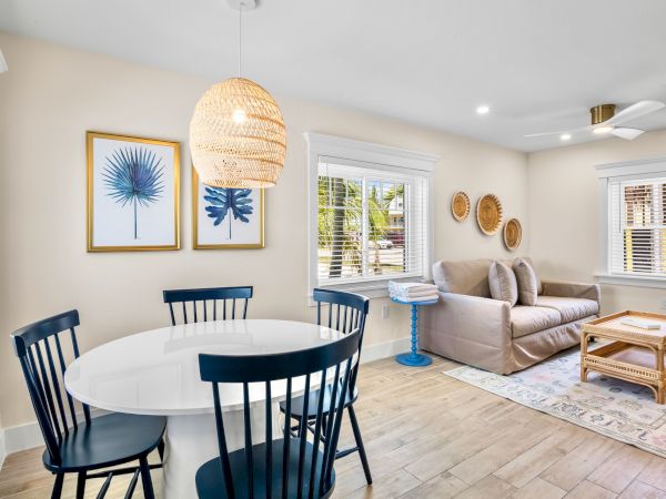 A bright living room with a sofa, wicker coffee table, dining set, and wall decor. Light decor creates an inviting space.