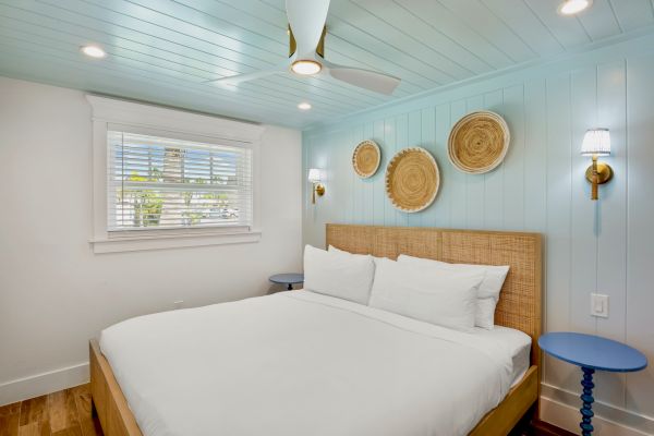A cozy bedroom with a woven headboard, circular wall decor, blue side tables, and soft lighting, featuring a large window and ceiling fan.