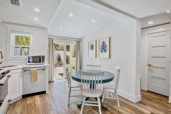 A bright kitchen with a microwave, a round table, three chairs, plant artwork, and a sliding door leading outside, accented by wood flooring.