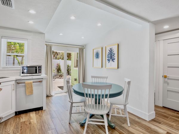 A bright kitchen with a microwave, a round table, three chairs, plant artwork, and a sliding door leading outside, accented by wood flooring.