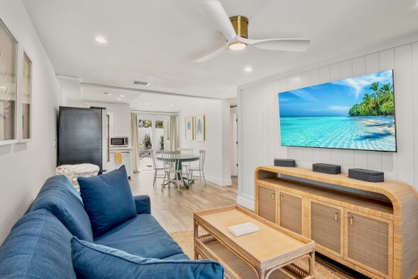 A cozy living room with a blue sofa, a TV displaying a beach scene, and a dining area in the background completes the scene.