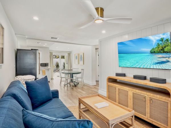 A cozy living room with a blue sofa, a TV displaying a beach scene, and a dining area in the background completes the scene.