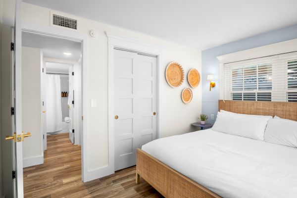 A modern bedroom with a wicker bed, wooden floors, and decorative plates on the wall. A doorway leads to a bathroom.