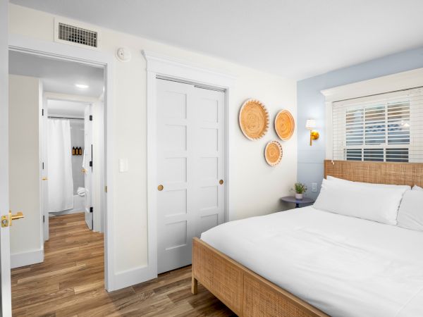 A modern bedroom with a wicker bed, wooden floors, and decorative plates on the wall. A doorway leads to a bathroom.