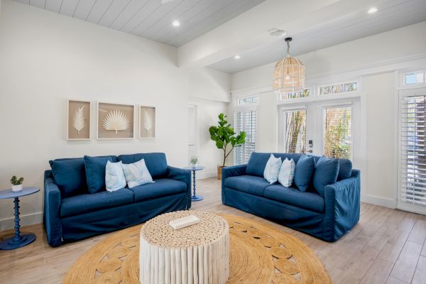 A cozy living room with two blue sofas, a round rug, wall art, and a plant, offering a bright and inviting atmosphere.