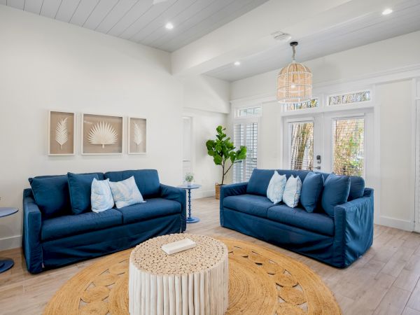A cozy living room with two blue sofas, a round rug, wall art, and a plant, offering a bright and inviting atmosphere.