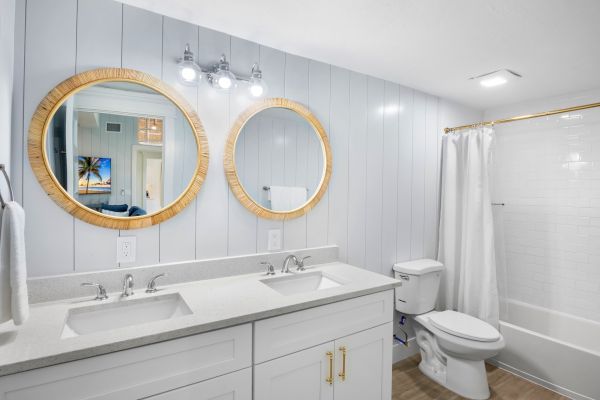 A modern bathroom features two round mirrors, dual sinks, a toilet, and a shower with a white curtain, accented by wood and light fixtures.