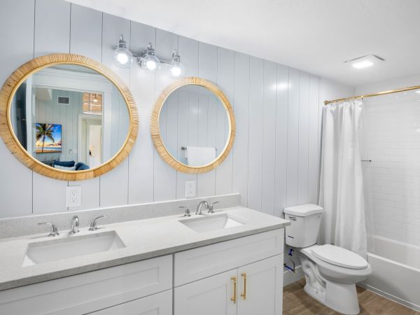A modern bathroom features two round mirrors, dual sinks, a toilet, and a shower with a white curtain, accented by wood and light fixtures.