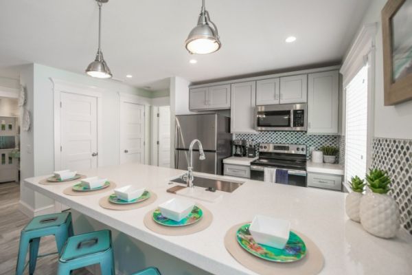 A modern kitchen with a center island, stools, and a dining setup. Stainless steel appliances and pendant lights enhance the sleek look.