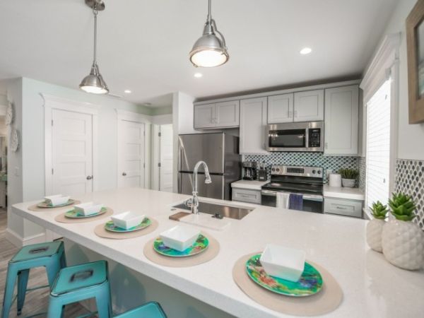 A modern kitchen with a center island, stools, and a dining setup. Stainless steel appliances and pendant lights enhance the sleek look.