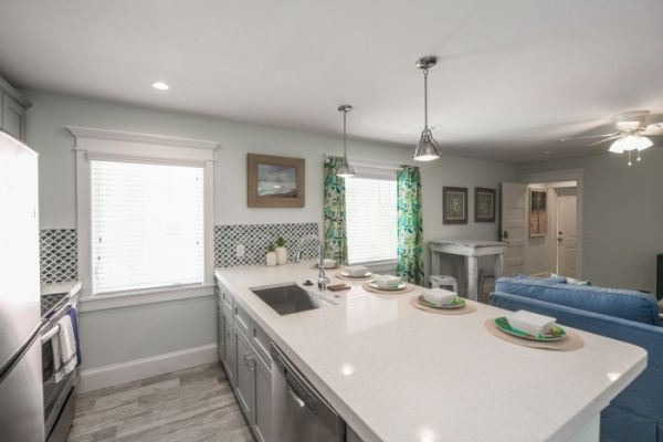 Modern kitchen with a large island, sink, and bar seating. Blue couch, patterned curtains, and light fixtures add style to the room.