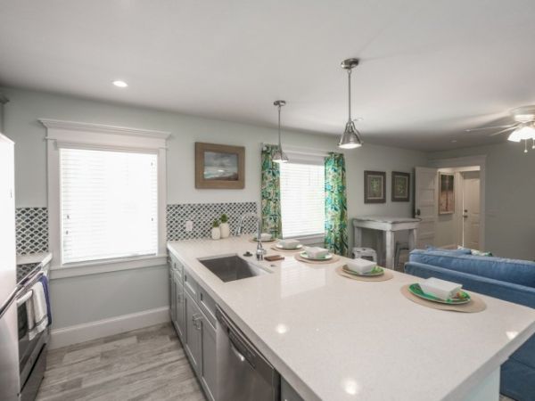 Modern kitchen with a large island, sink, and bar seating. Blue couch, patterned curtains, and light fixtures add style to the room.
