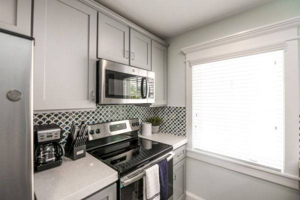 A modern kitchen with white cabinets, stainless steel appliances, a fish-scale backsplash, and a window with blinds.