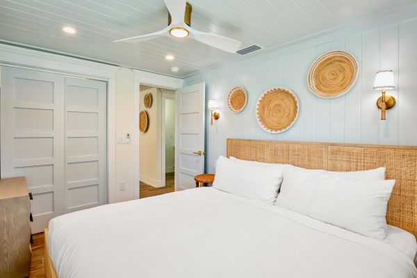 A cozy bedroom with a bed, woven wall decor, white and wood accents, sliding closet doors, and a ceiling fan.