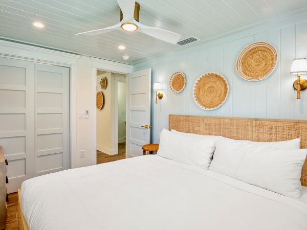 A cozy bedroom with a bed, woven wall decor, white and wood accents, sliding closet doors, and a ceiling fan.