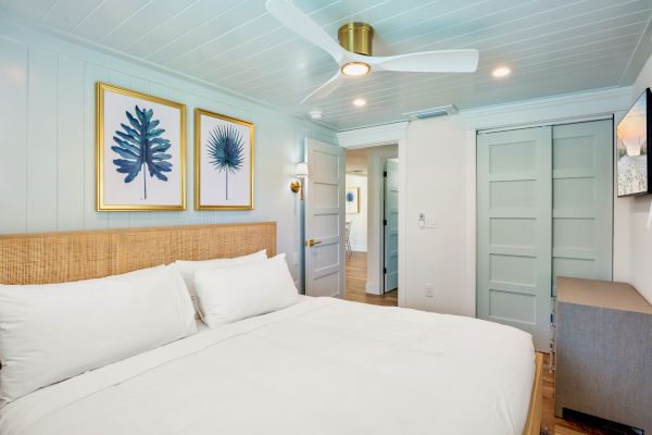 A cozy bedroom with a comfy bed, art on the wall, ceiling fan, and natural decor touches.