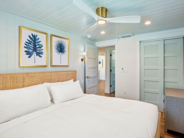 A cozy bedroom with a comfy bed, art on the wall, ceiling fan, and natural decor touches.