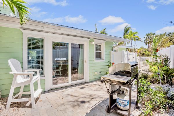 A serene backyard with a green house, a propane barbecue grill, and patio furniture in a sunny garden setting.