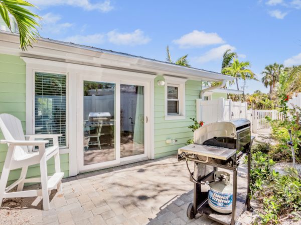A serene backyard with a green house, a propane barbecue grill, and patio furniture in a sunny garden setting.