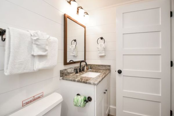 A modern bathroom with a marble countertop, sink, mirror, and white door. Towels hang on the wall and toilet paper rolls are visible.